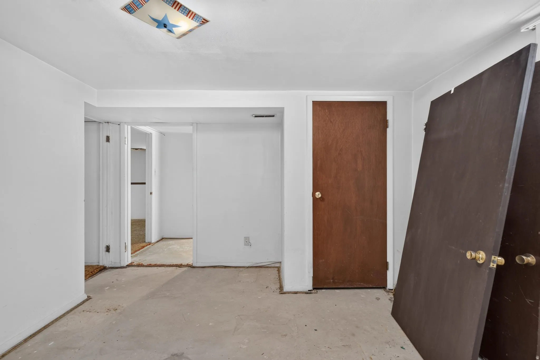 Unfinished room featuring white walls, a wood-finish door, and concrete flooring