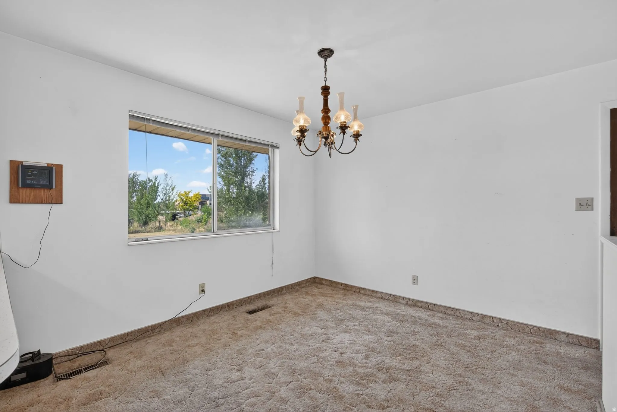 Spacious room featuring a central chandelier, a large window, wall-to-wall carpeting, and baseboard trim