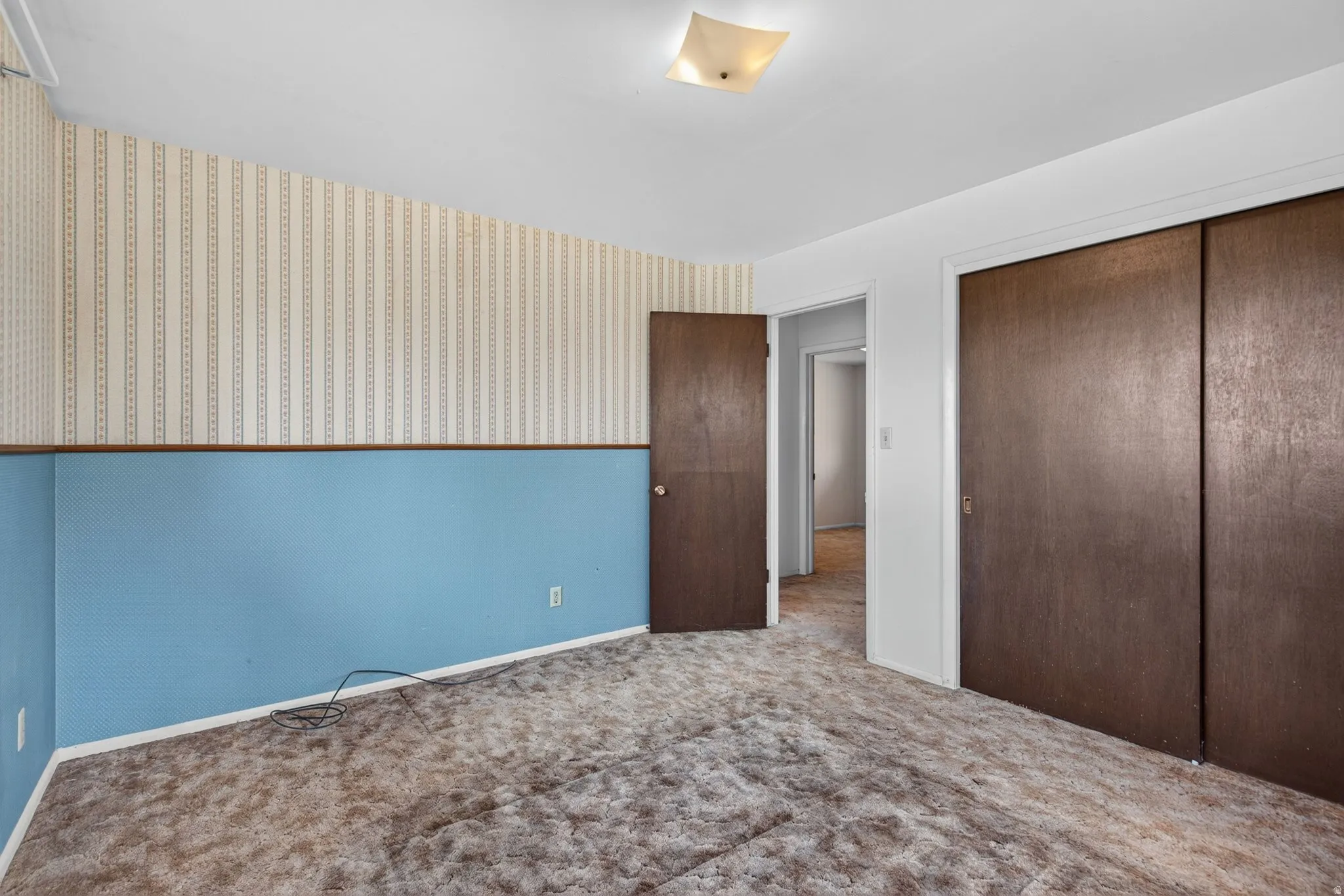 Carpeted room featuring a ceiling-mounted light fixture, two-tone wall treatment with a patterned upper section, and two large closet doors