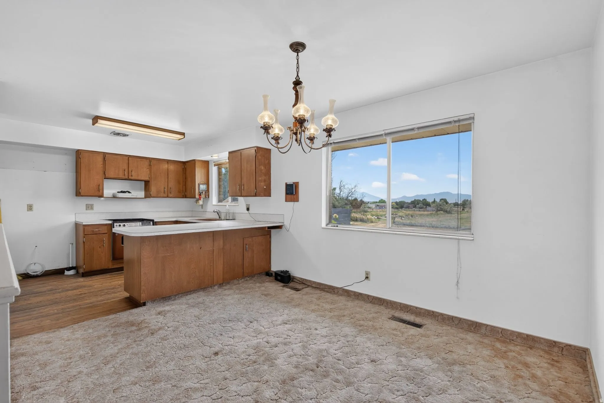 Open-concept kitchen and dining area featuring wood cabinetry, white countertops, built-in range, and a window with mountain scenery