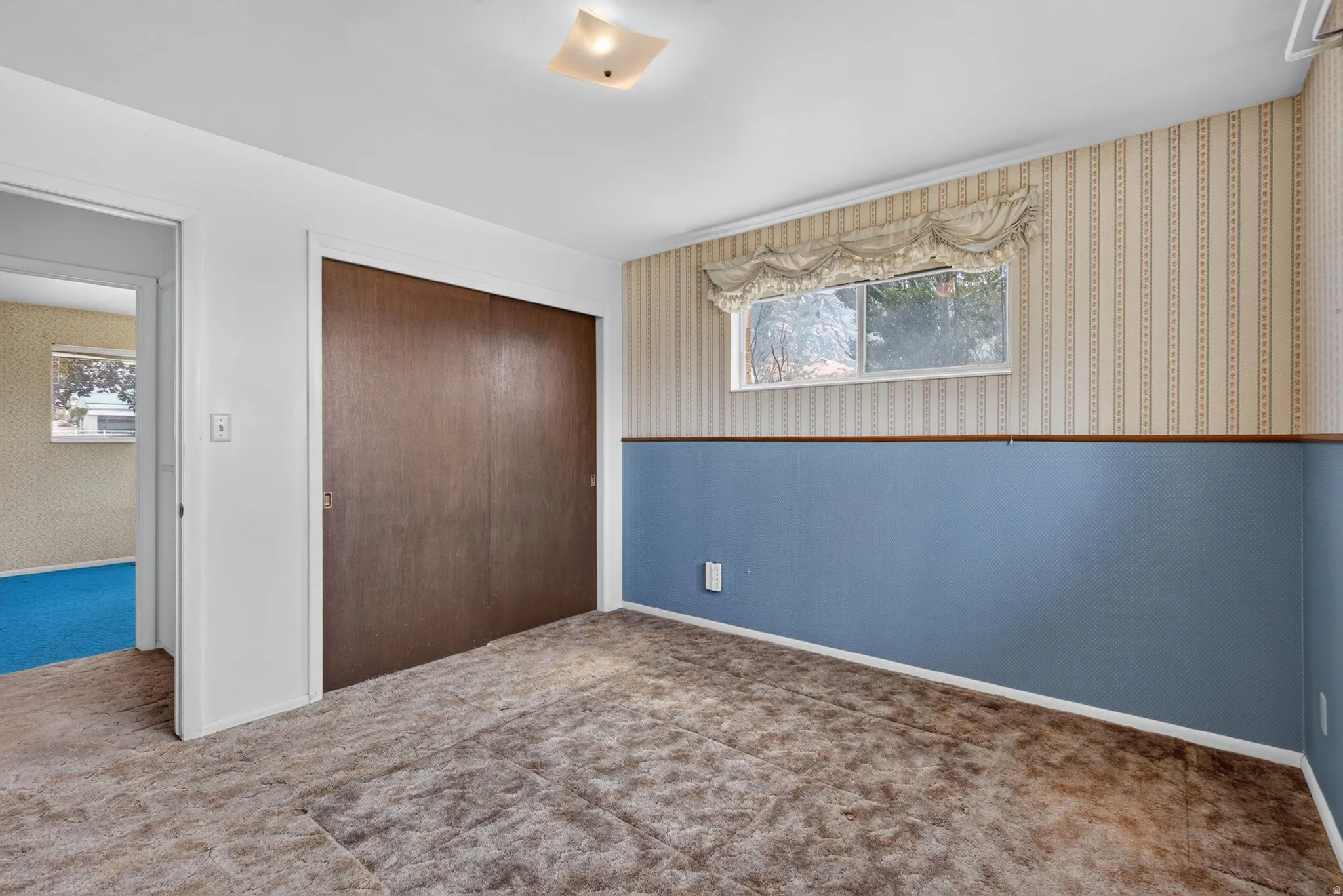 Carpeted room featuring a window with a valance, a full-size closet with sliding wood doors, and a wall with blue paneling