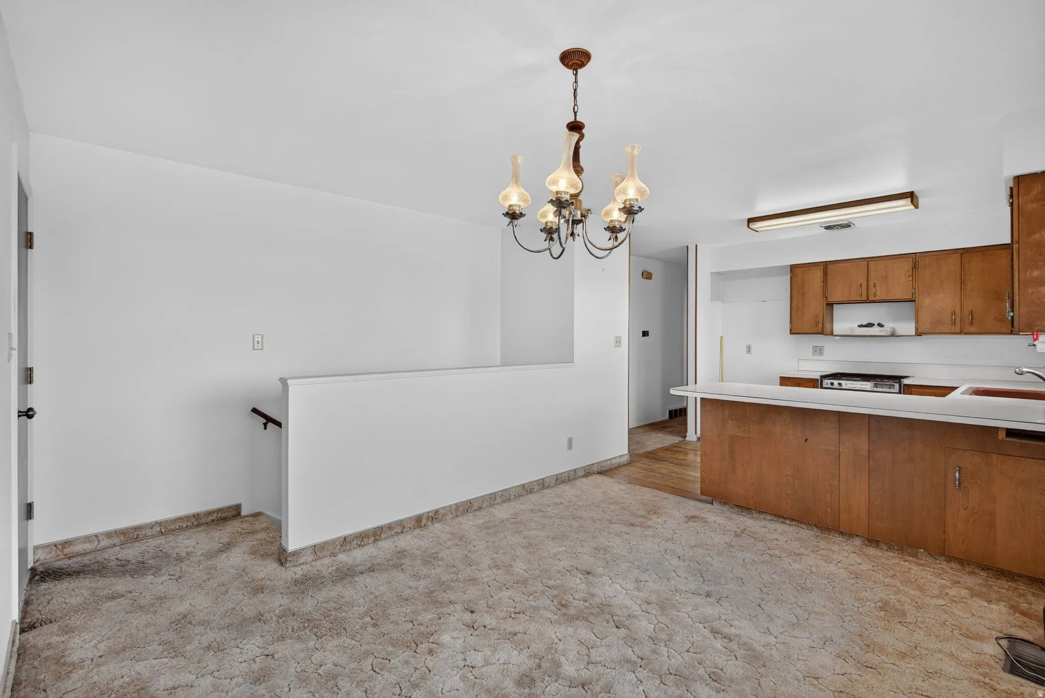 Open concept living space featuring a vintage chandelier, kitchen with wood cabinetry, and a white countertop bar