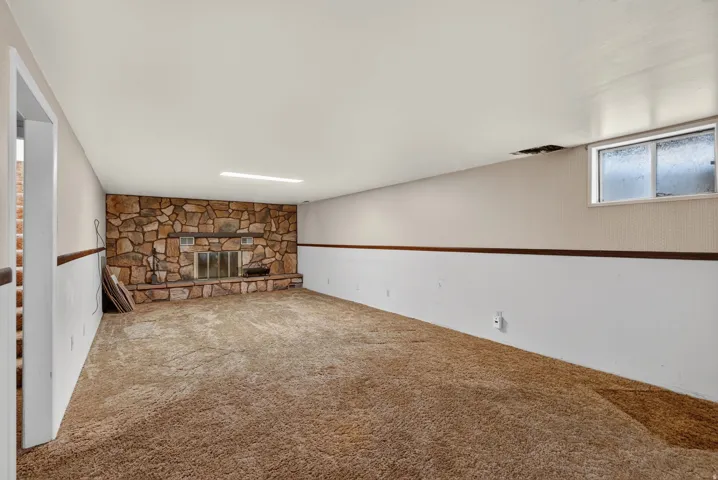Spacious room featuring a stone-clad fireplace with a hearth and a metal screen, plush carpeting, and wainscoting with a wood trim