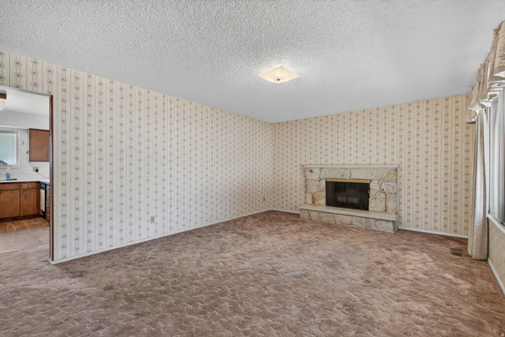 Living area featuring a stone fireplace with hearth, textured carpeting, patterned wallpaper, and a flush-mount ceiling light fixture