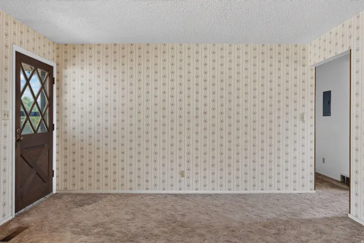 Entryway featuring a diamond-paneled dark wood door, patterned wallpaper, textured ceiling, and brown carpet