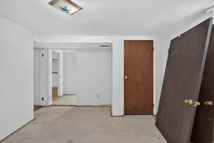 Unfinished room featuring white walls, a wood-finish door, and concrete flooring