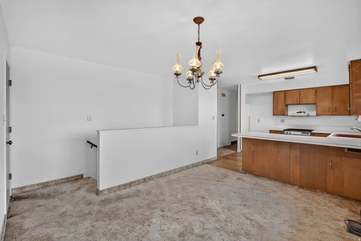 Open concept living space featuring a vintage chandelier, kitchen with wood cabinetry, and a white countertop bar