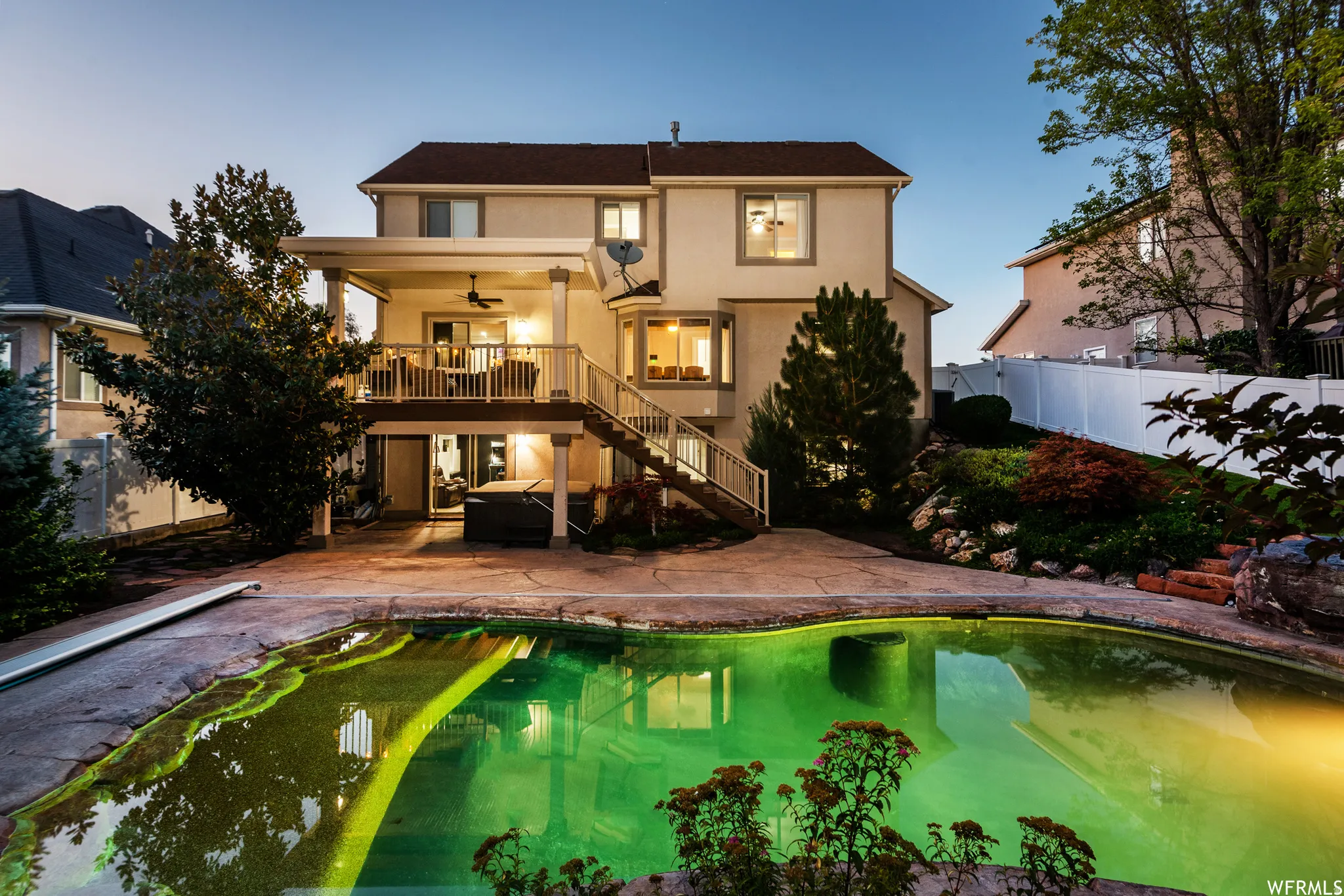 Rear exterior featuring a freeform swimming pool, concrete patio, multi-level deck with columns, and a terraced landscaped hillside