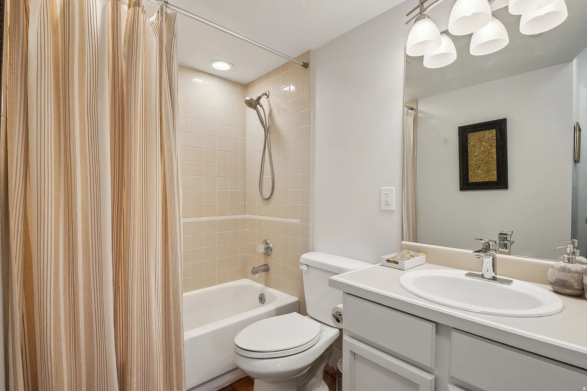 Full bathroom featuring a white porcelain tub, light-toned tiled shower surround, recessed ceiling lighting, and a vanity with an integrated sink and base cabinetry