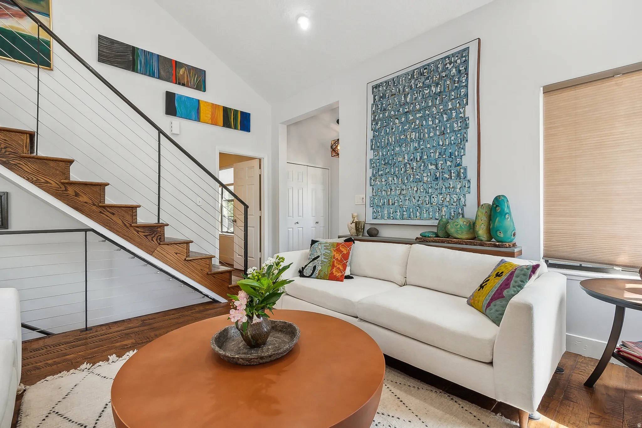 Living area with vaulted ceilings, wood-finish flooring, and a contemporary cable railing staircase with wood treads.  The two couches are removed, call for details.
