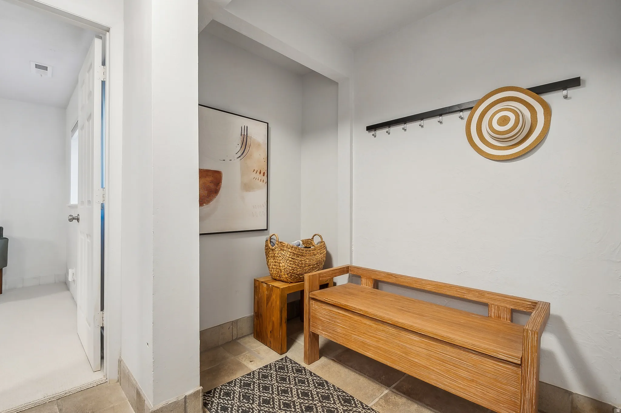 Entryway featuring light-toned flooring, a light wood-finish storage bench, and a wall-mounted coat rack