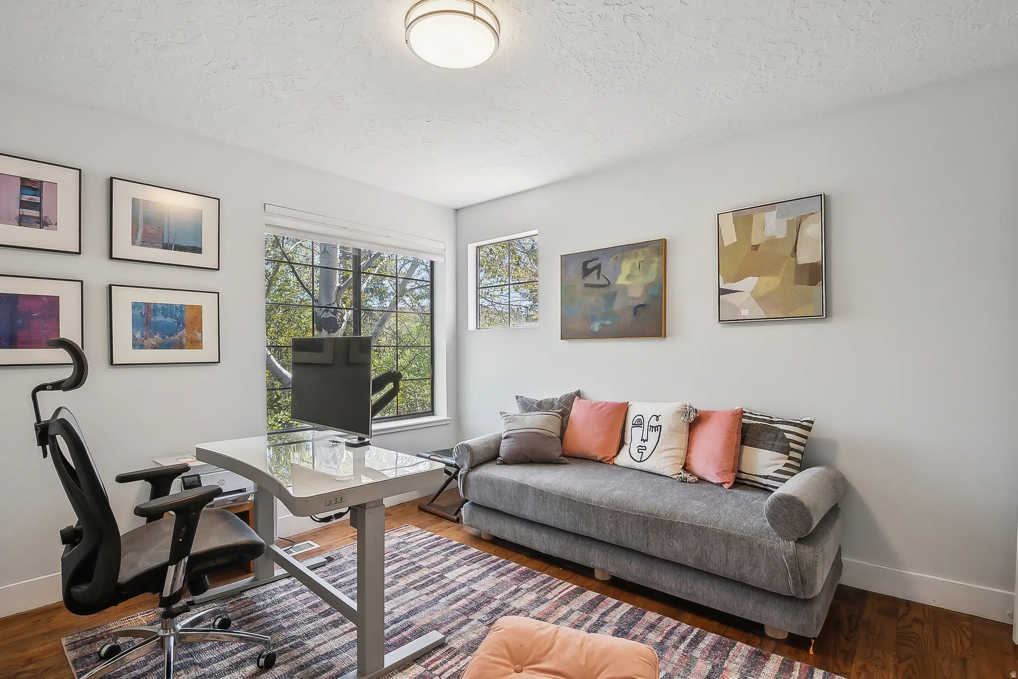 Versatile room featuring hardwood flooring, multiple windows providing natural light, recessed ceiling light fixture, and a neutral wall color