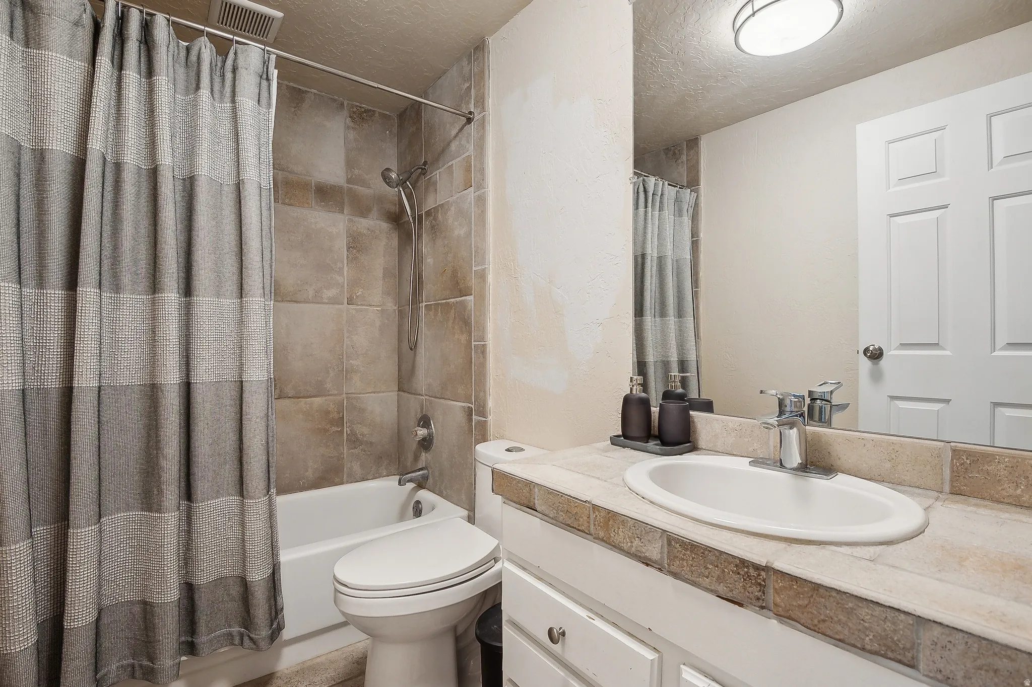Bathroom featuring a tiled shower surround, white bathtub, and a vanity with a tile countertop