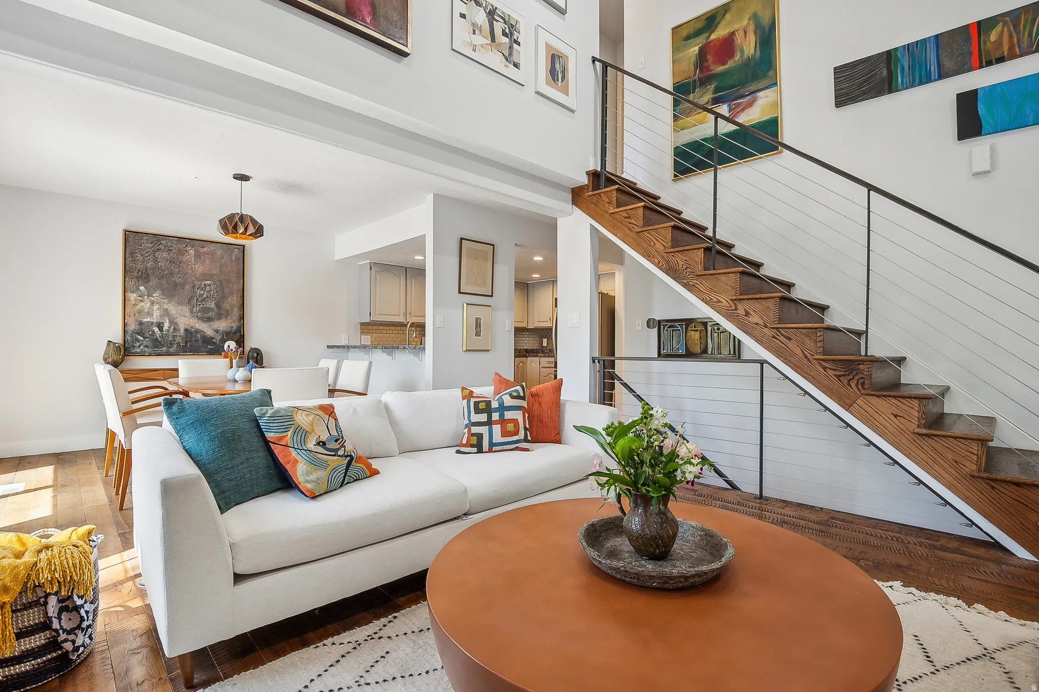 Open-concept living area featuring high ceilings, wood-finish flooring, and a modern staircase with cable railing.  The two couches are removed, call for details.