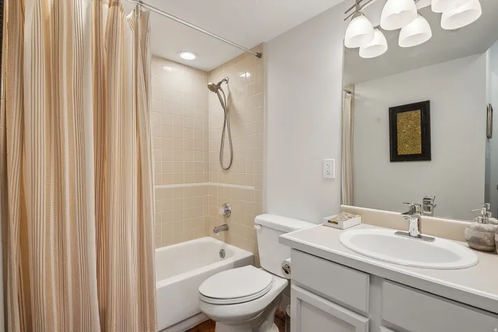 Full bathroom featuring a white porcelain tub, light-toned tiled shower surround, recessed ceiling lighting, and a vanity with an integrated sink and base cabinetry