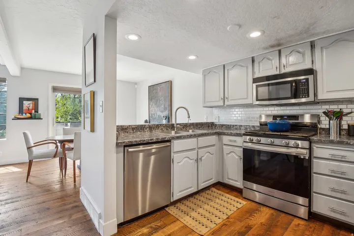 Kitchen featuring light gray cabinetry, stainless steel appliances, a subway tile backsplash, and wood-finish flooring