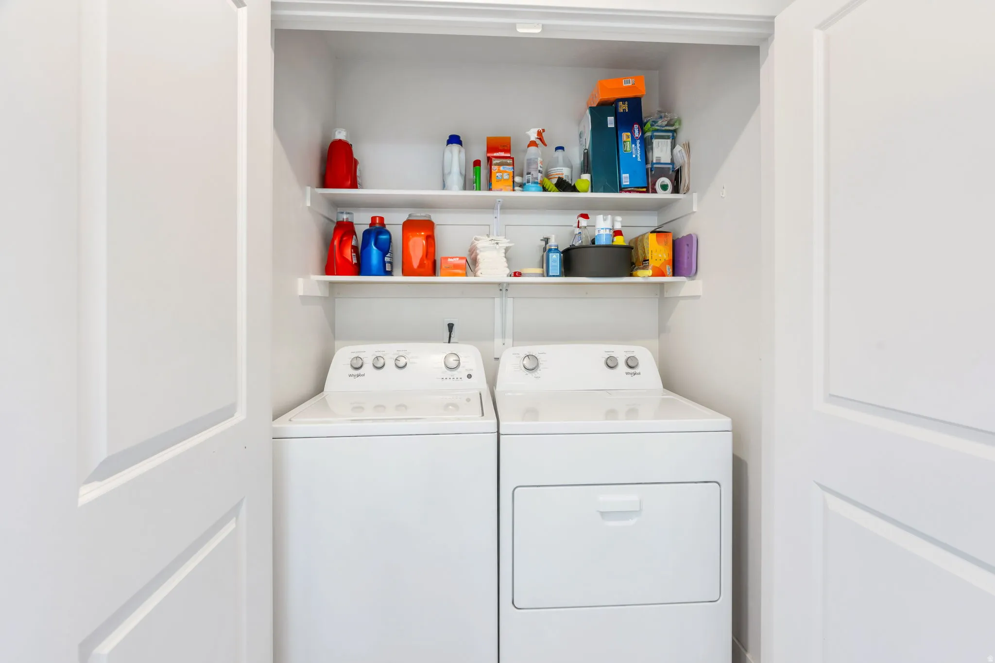 Dedicated laundry area featuring a white washing machine, matching dryer, and built-in white shelving