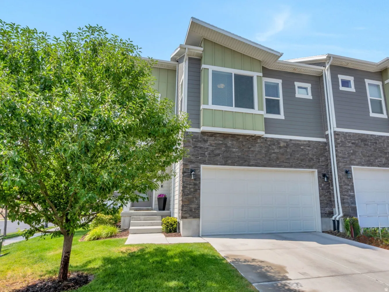 2-car garage, stone and siding facade, mature landscaping, and concrete driveway