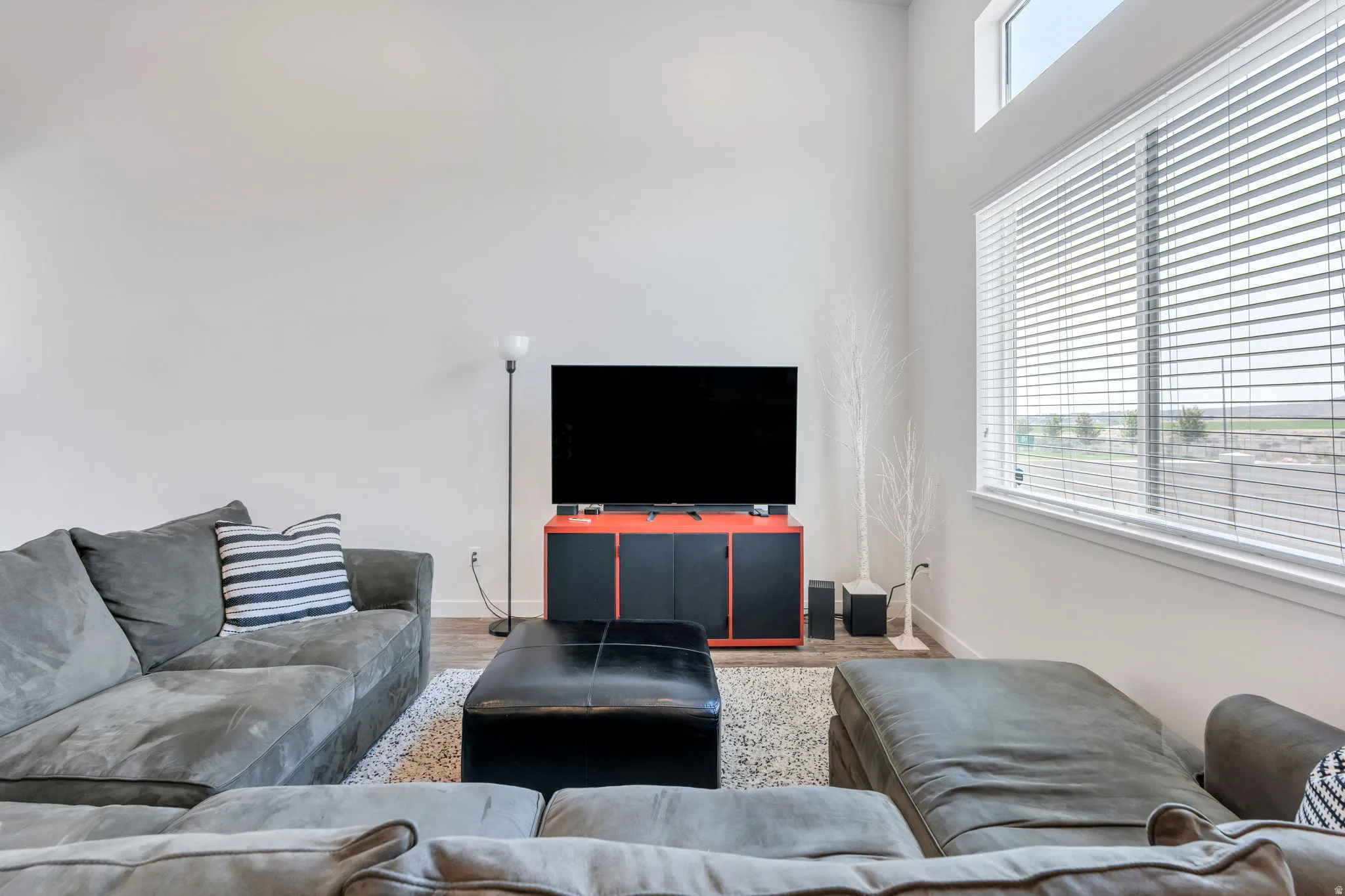 Spacious living area featuring high ceilings, a large window with blinds, and an upper transom window