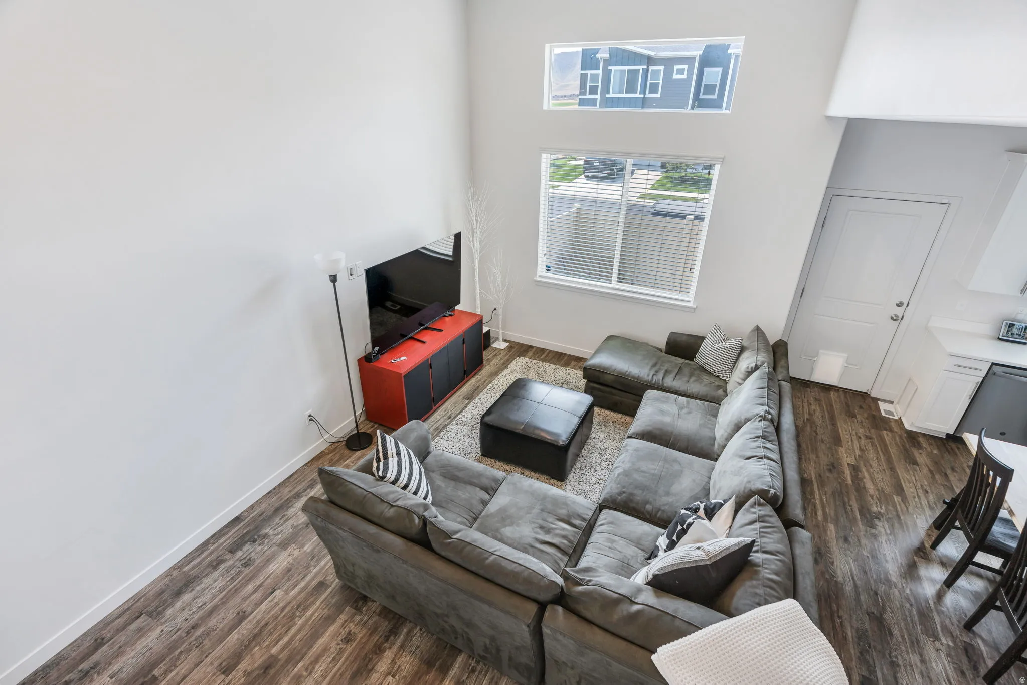 Vaulted ceilings with high windows, wood-finish flooring, white walls, and a contemporary open-concept layout