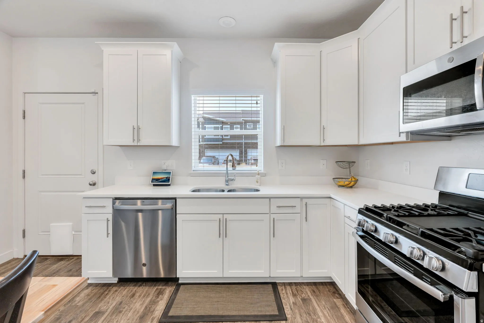 Kitchen featuring white cabinetry, stainless steel appliances, wood-finish flooring, and a double basin sink