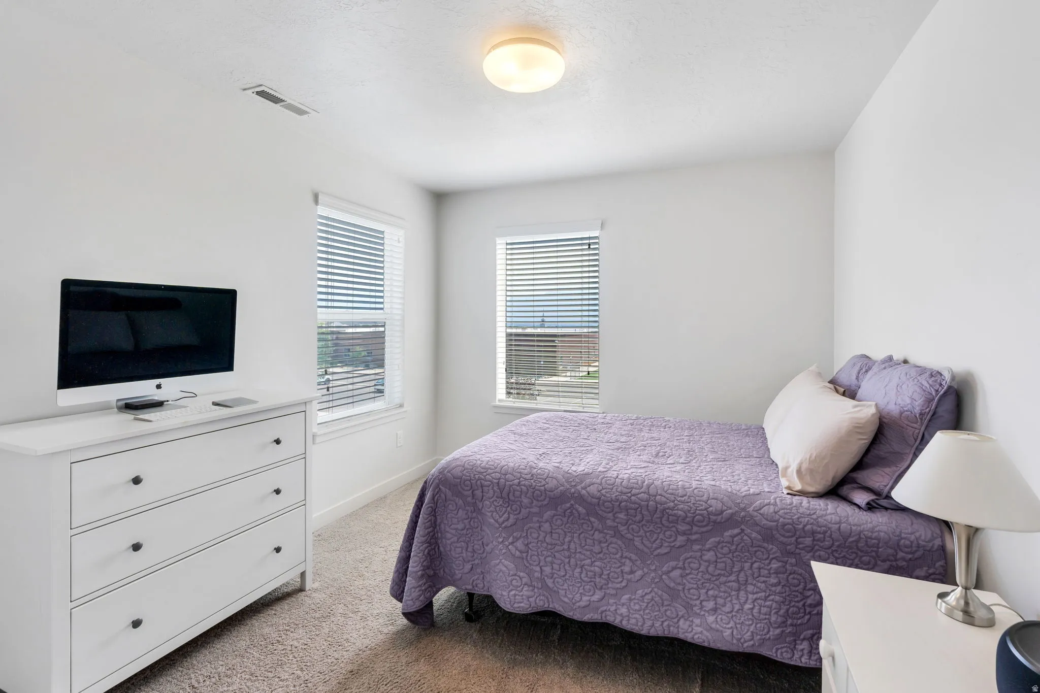 2nd Bedroom featuring two windows with horizontal blinds, neutral carpet flooring, and a flush-mount ceiling light fixture