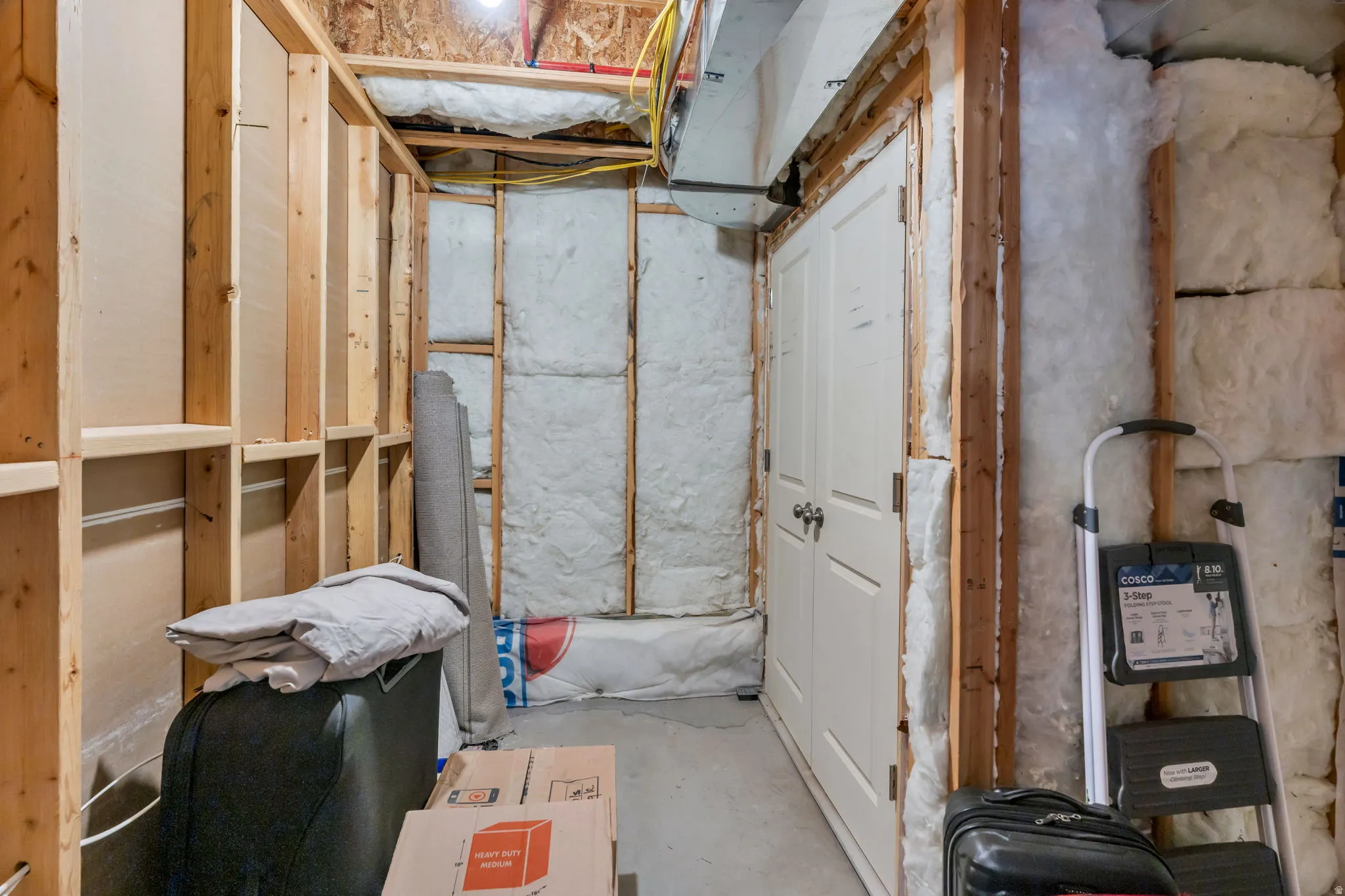 Unfinished basement area for storage featuring wood framing, white insulation, a utility door, and a concrete floor