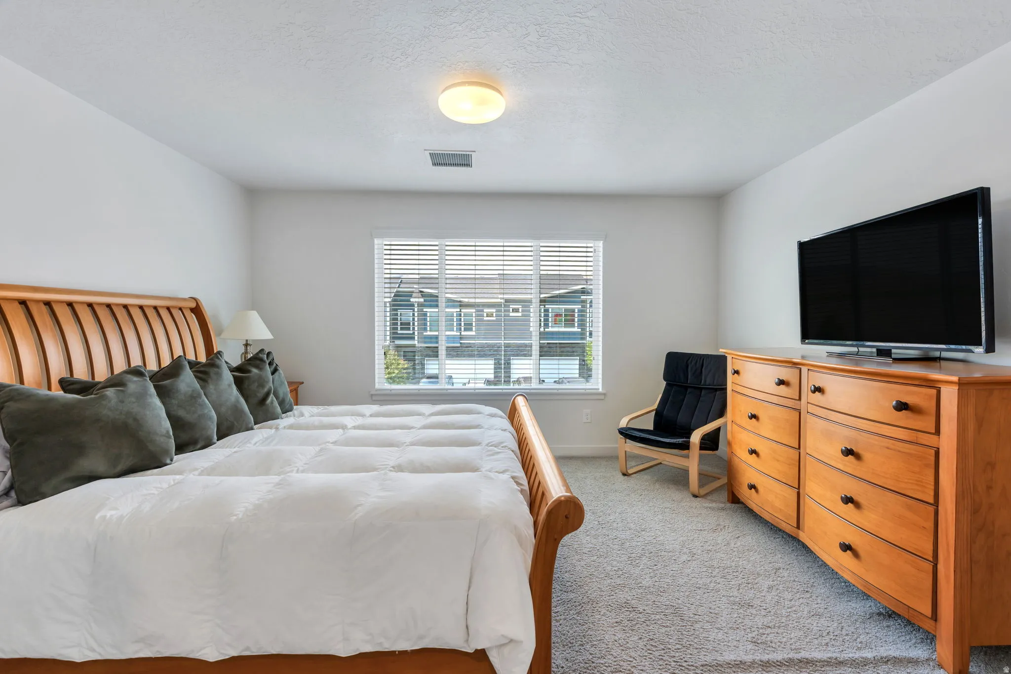 Spacious primary bedroom featuring light neutral wall tones, a large window with blinds, and light-colored carpet flooring