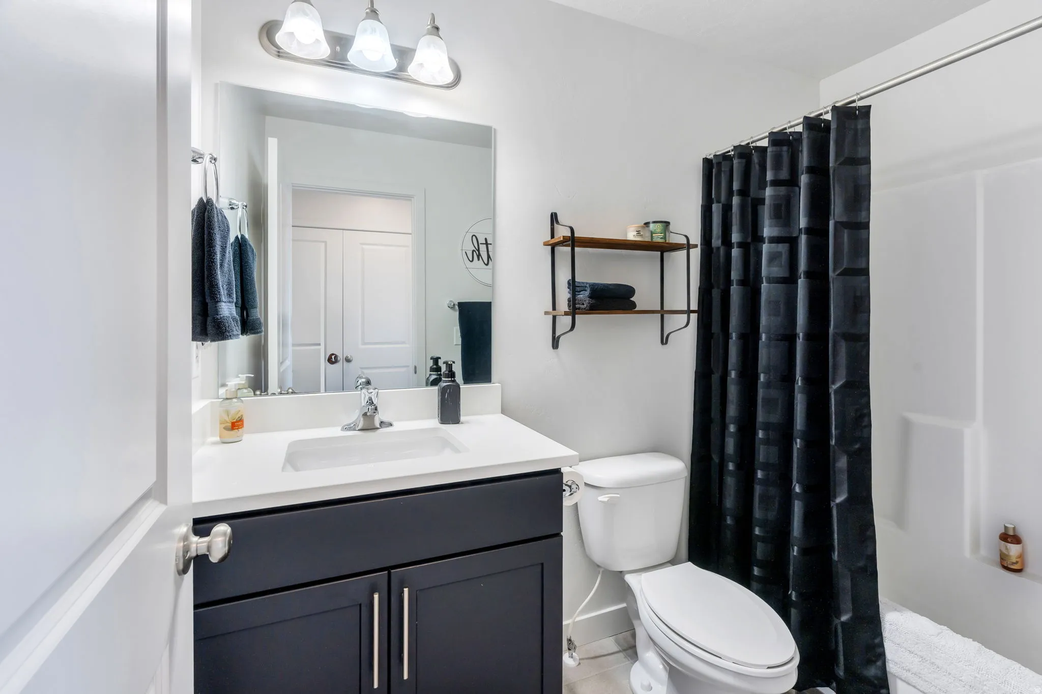 Full bathroom featuring a single vanity with a white countertop, undermount sink, and dark cabinetry