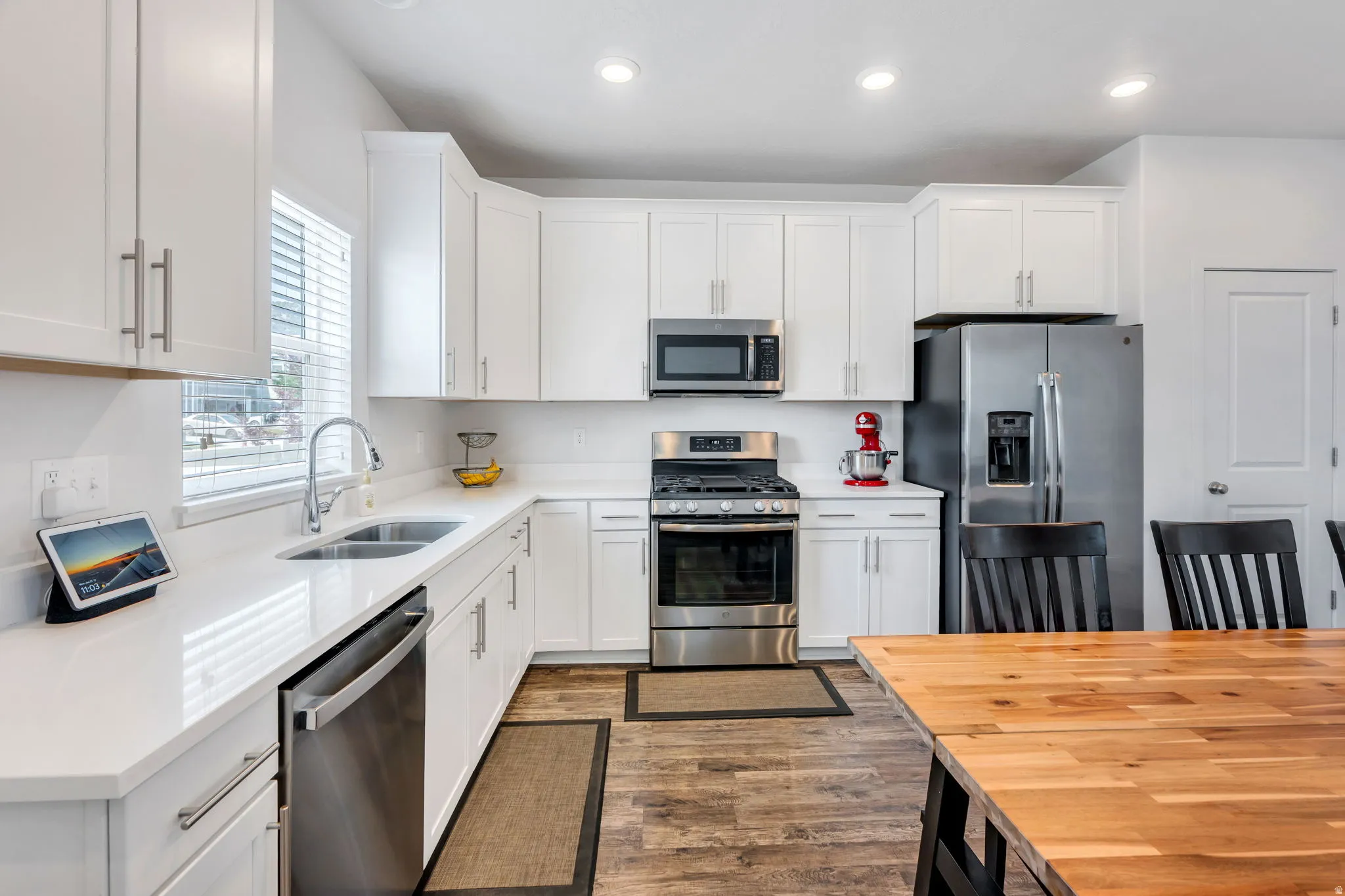 Bright kitchen featuring white cabinetry, stainless steel appliances, light countertops, a dual basin sink, and wood-finish flooring