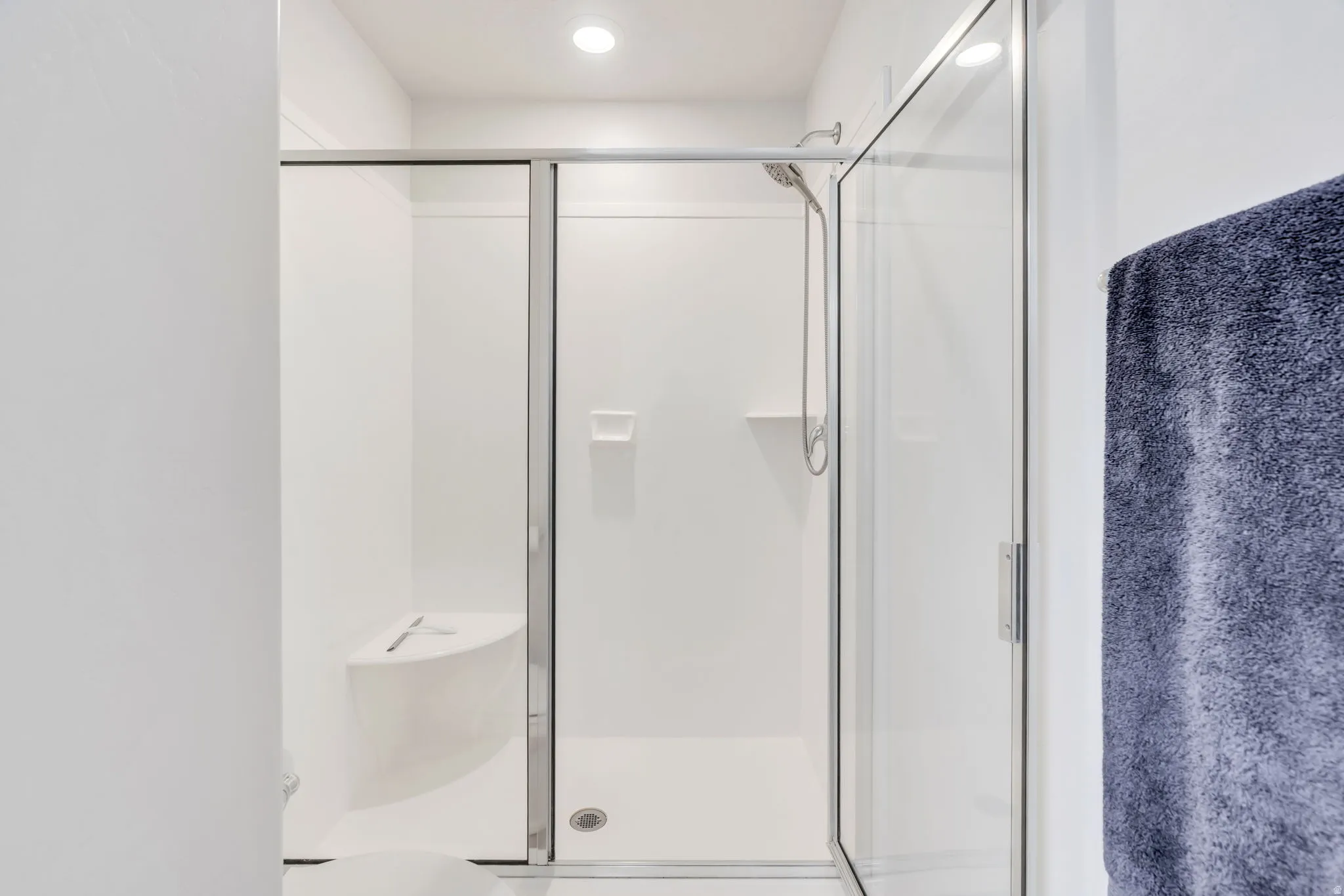 White shower enclosure featuring glass sliding doors and a built-in corner bench