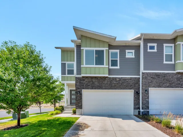 Contemporary townhome facade featuring multi-tone siding, stone accents, a private front entrance, and an attached two-car garage