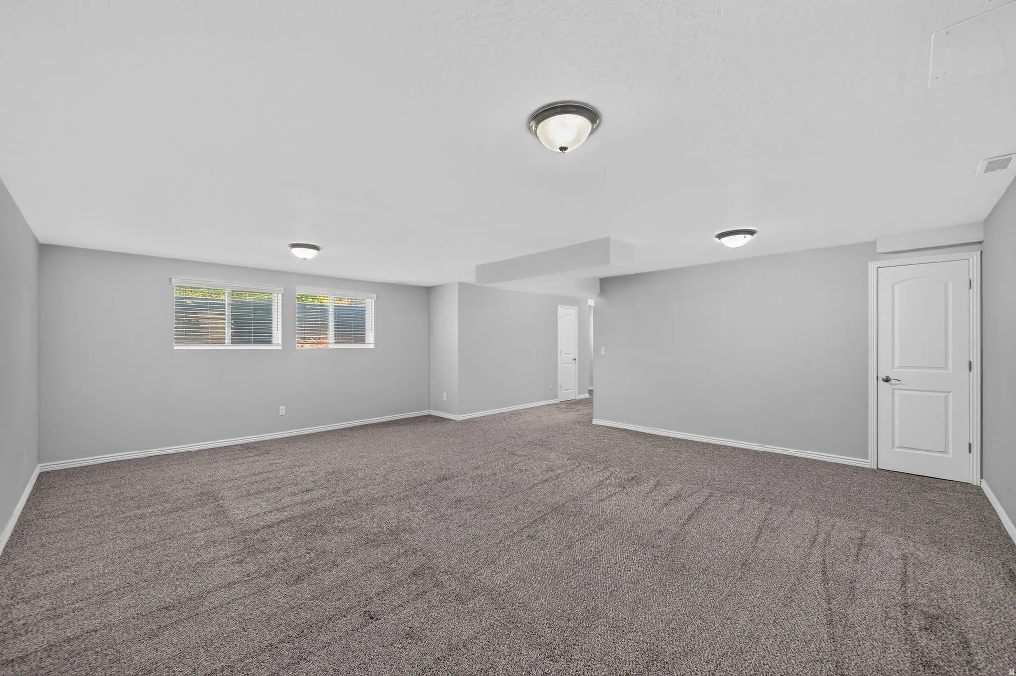 Spacious room with new carpeting, light gray walls, and multiple windows