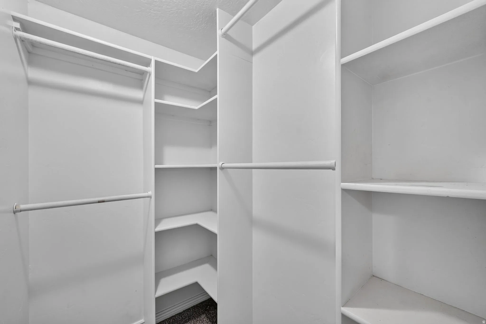 Master closet featuring multiple hanging rods, built-in shelving, corner shelves, and a textured ceiling