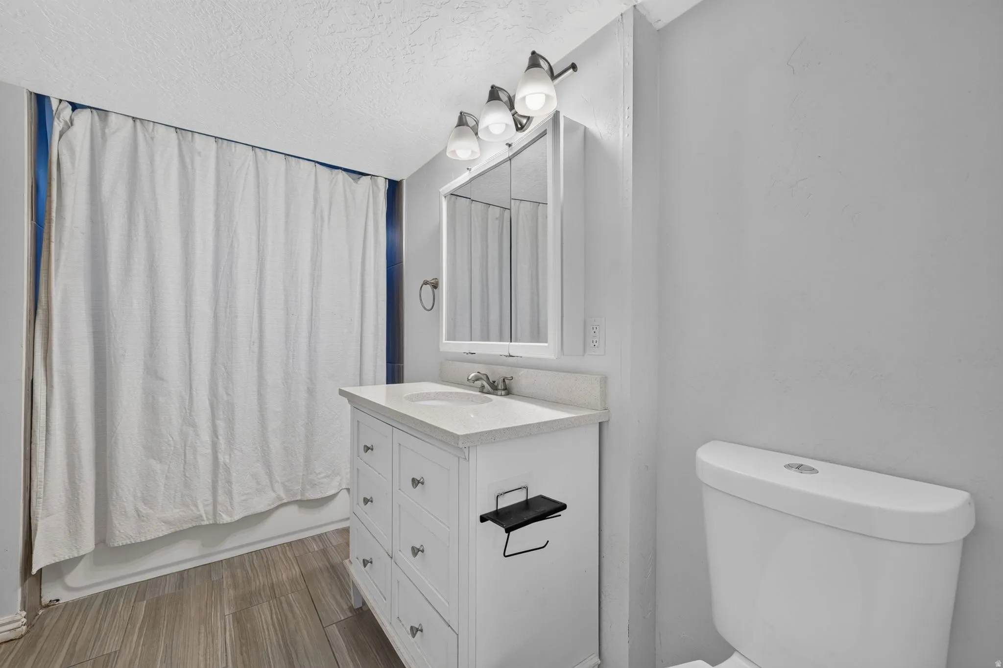 downstairs Bathroom featuring a white vanity with an integrated sink, a white toilet, and wood-finish flooring