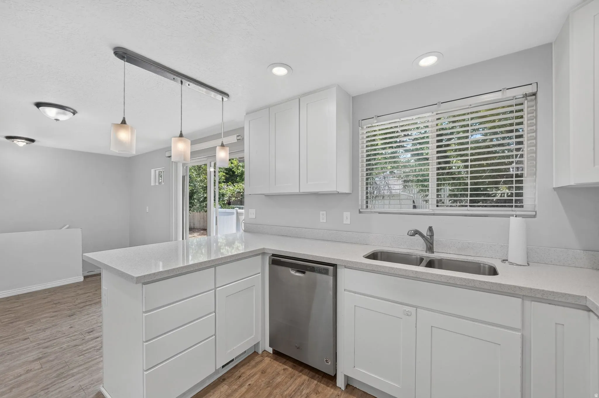 Modern kitchen featuring white shaker cabinetry, light-toned countertops, a stainless steel double sink, and a stainless steel dishwasher