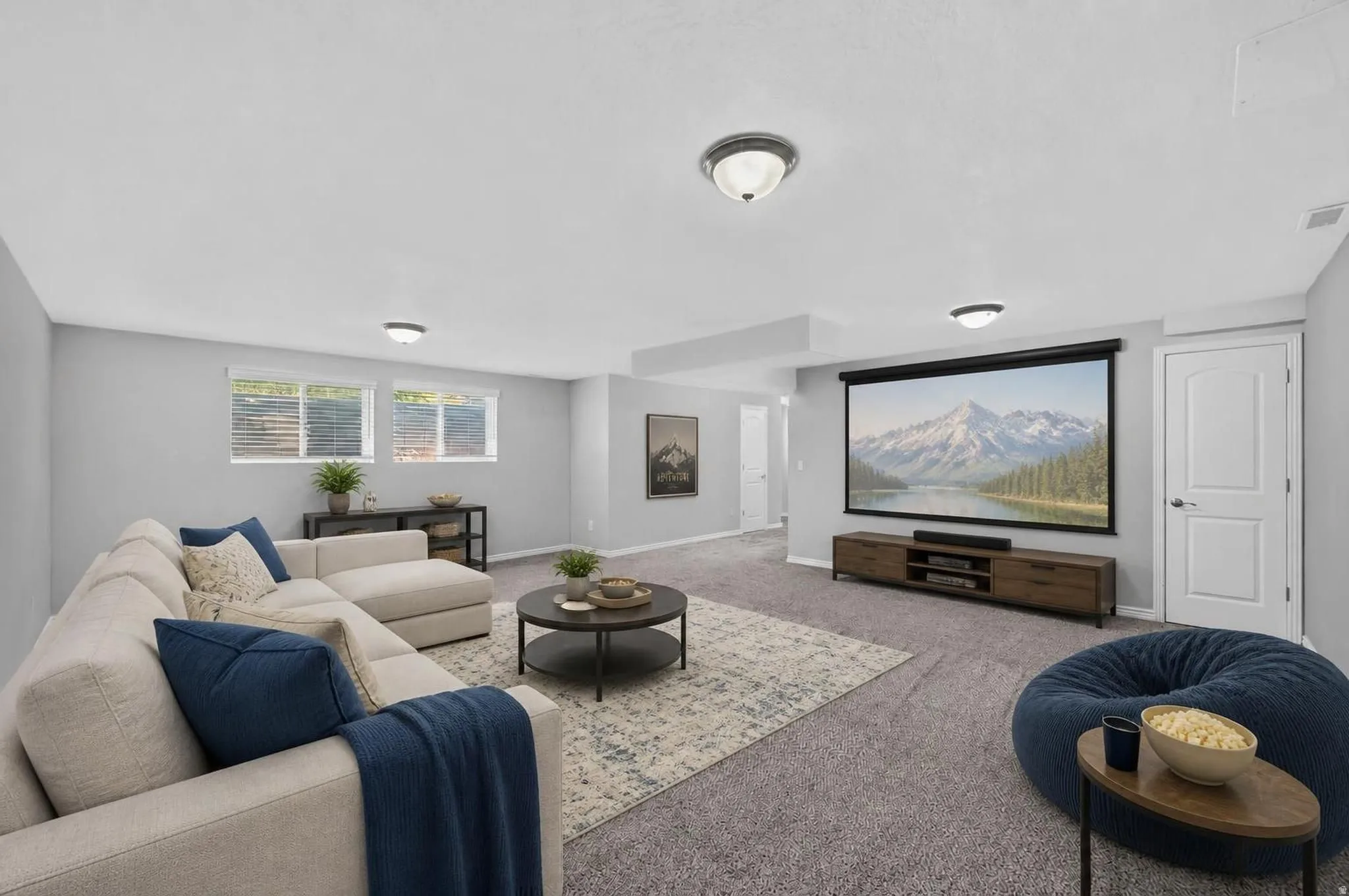 Spacious lower-level living area featuring neutral carpeting, a large projection screen, and a media console