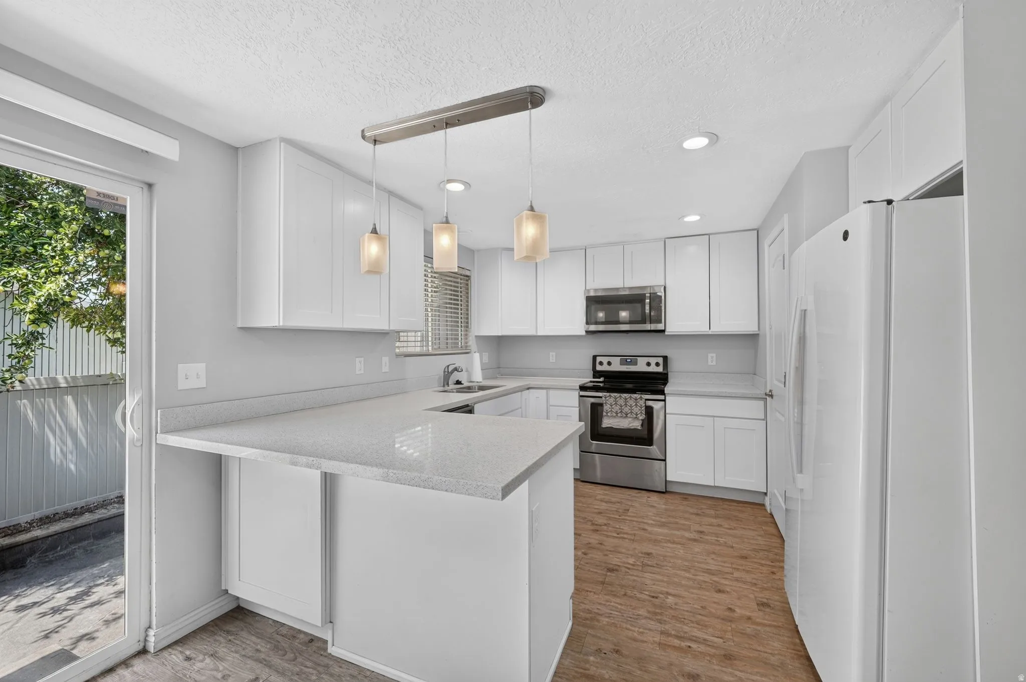 Modern kitchen featuring white cabinetry, light-toned countertops, stainless steel appliances, and wood-finish flooring