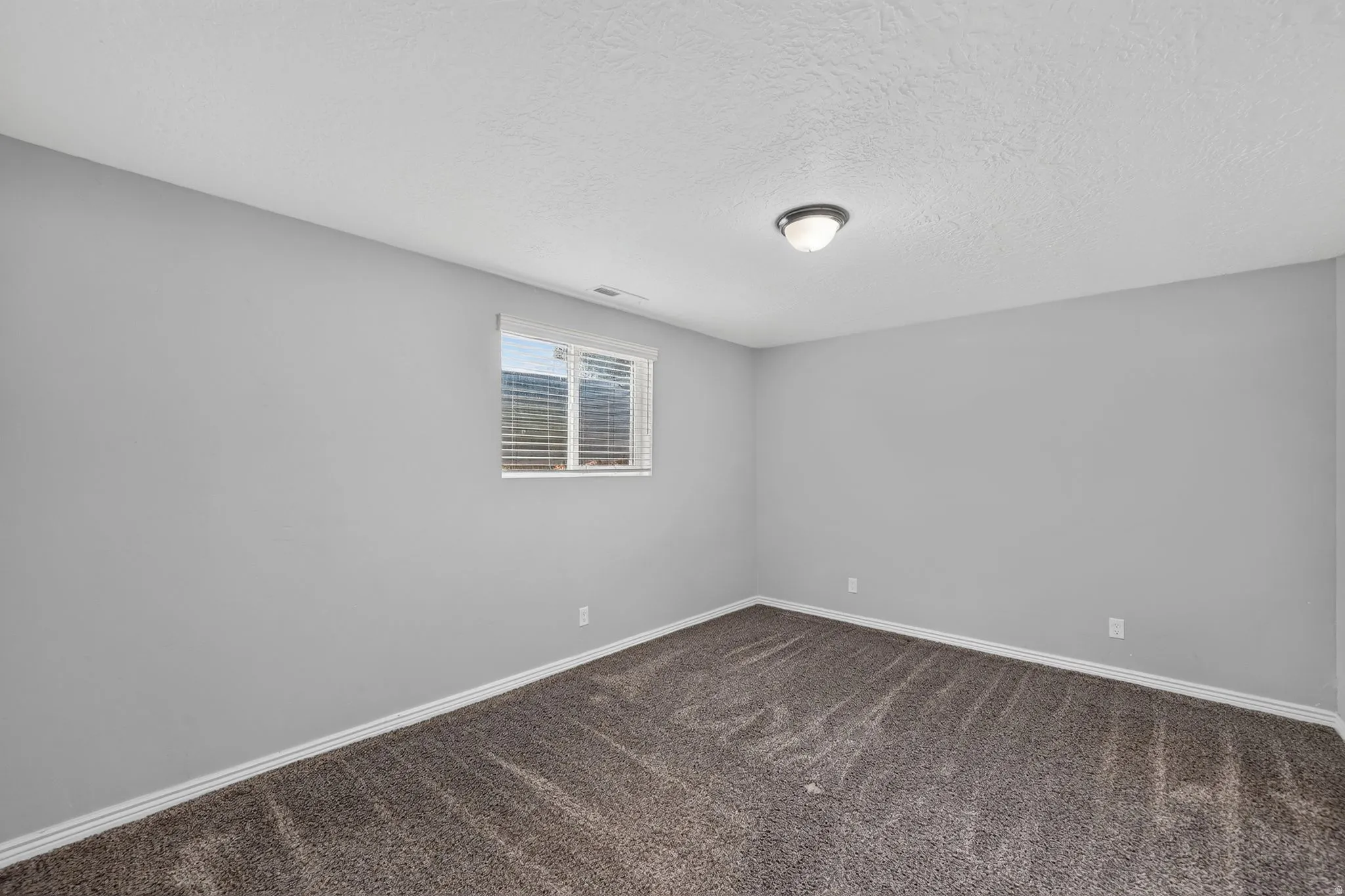 Carpeted room featuring light gray walls, white baseboards, and a window with blinds