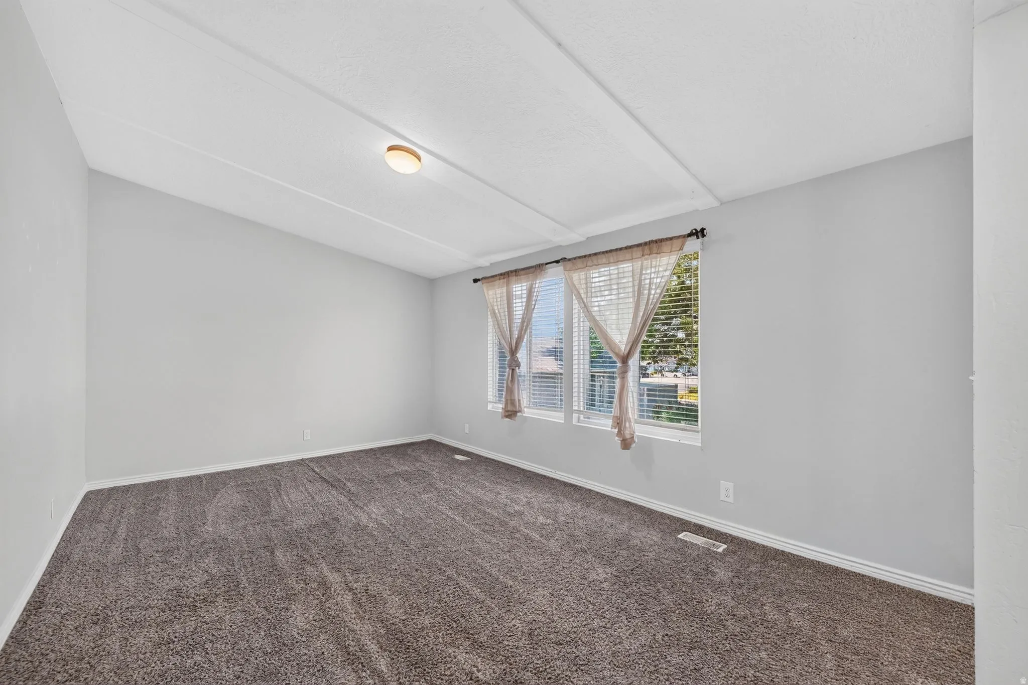 Spacious room featuring gray carpet flooring, light gray wall paint, and a sloped ceiling with a flush-mount light fixture