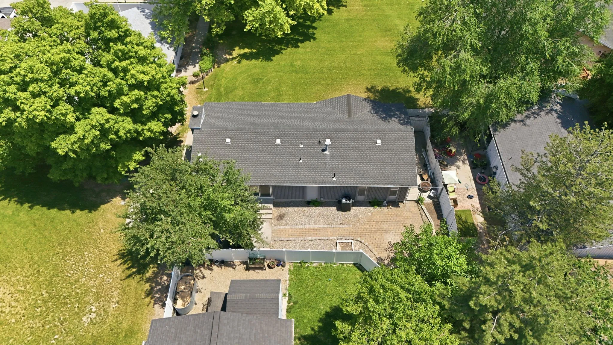 Single-story residence featuring a dark shingle roof, a gravel patio area, and a green lawn