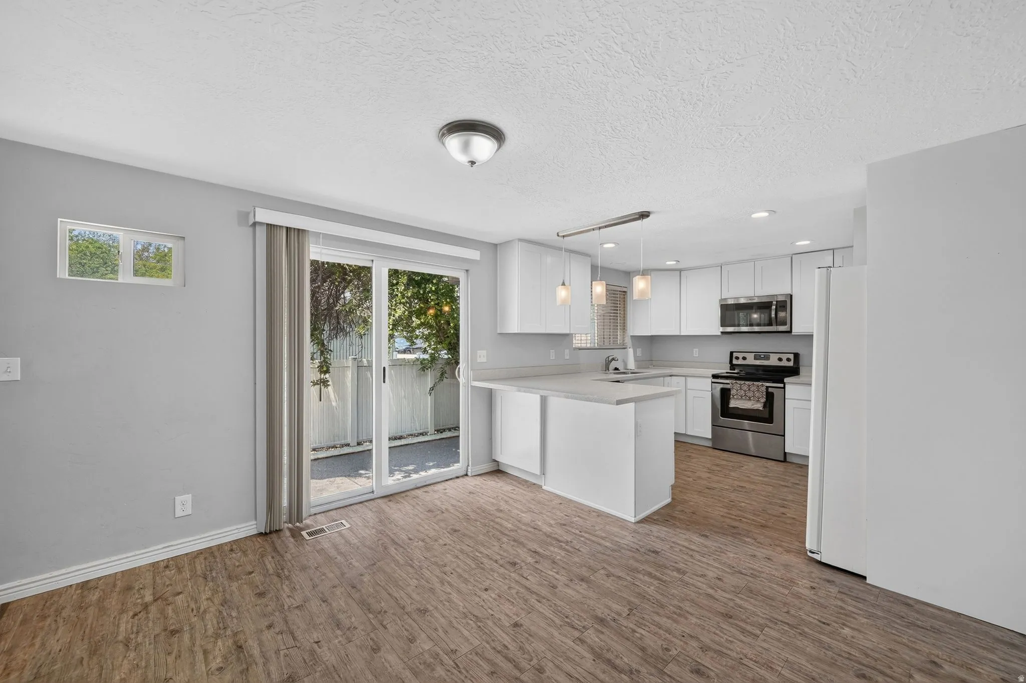 Kitchen and dining area featuring wood-finish flooring, white cabinetry, stainless steel appliances, and a sliding glass door