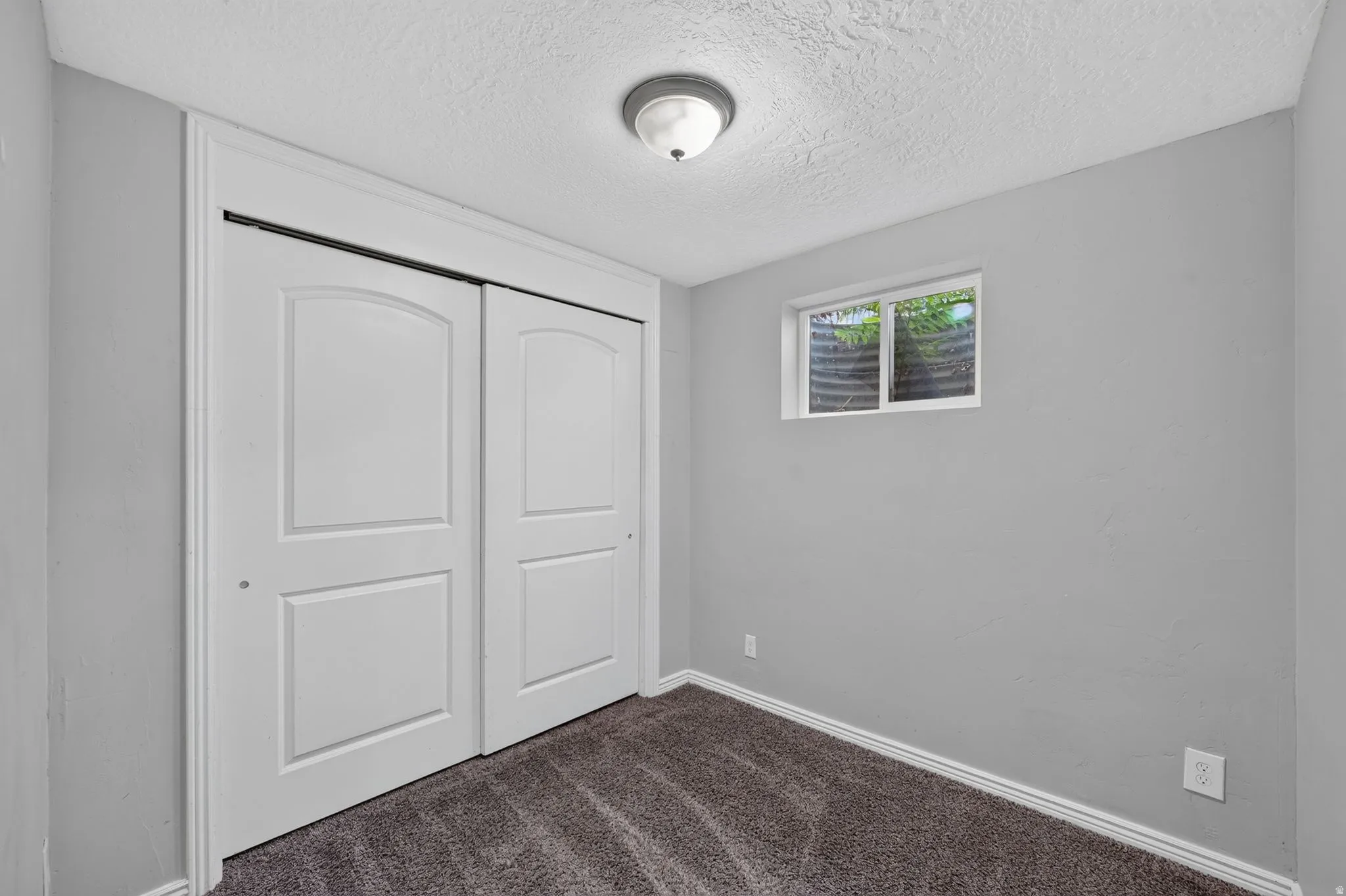 Interior space featuring a window with a window well, light gray walls, white trim, and dark gray carpet flooring