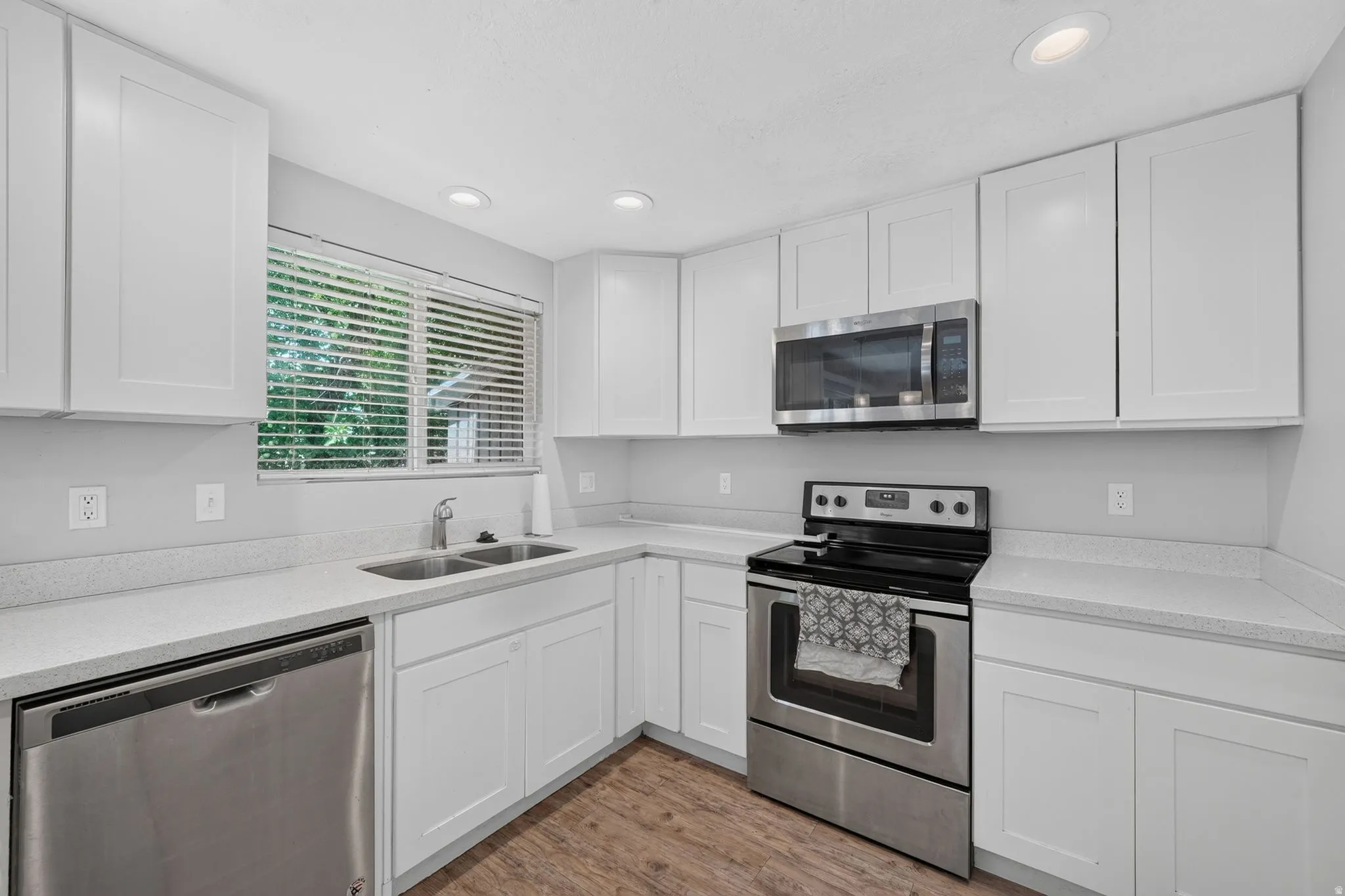 Kitchen featuring white shaker-style cabinetry, stainless steel appliances, speckled countertops, a double basin sink, and recessed lighting