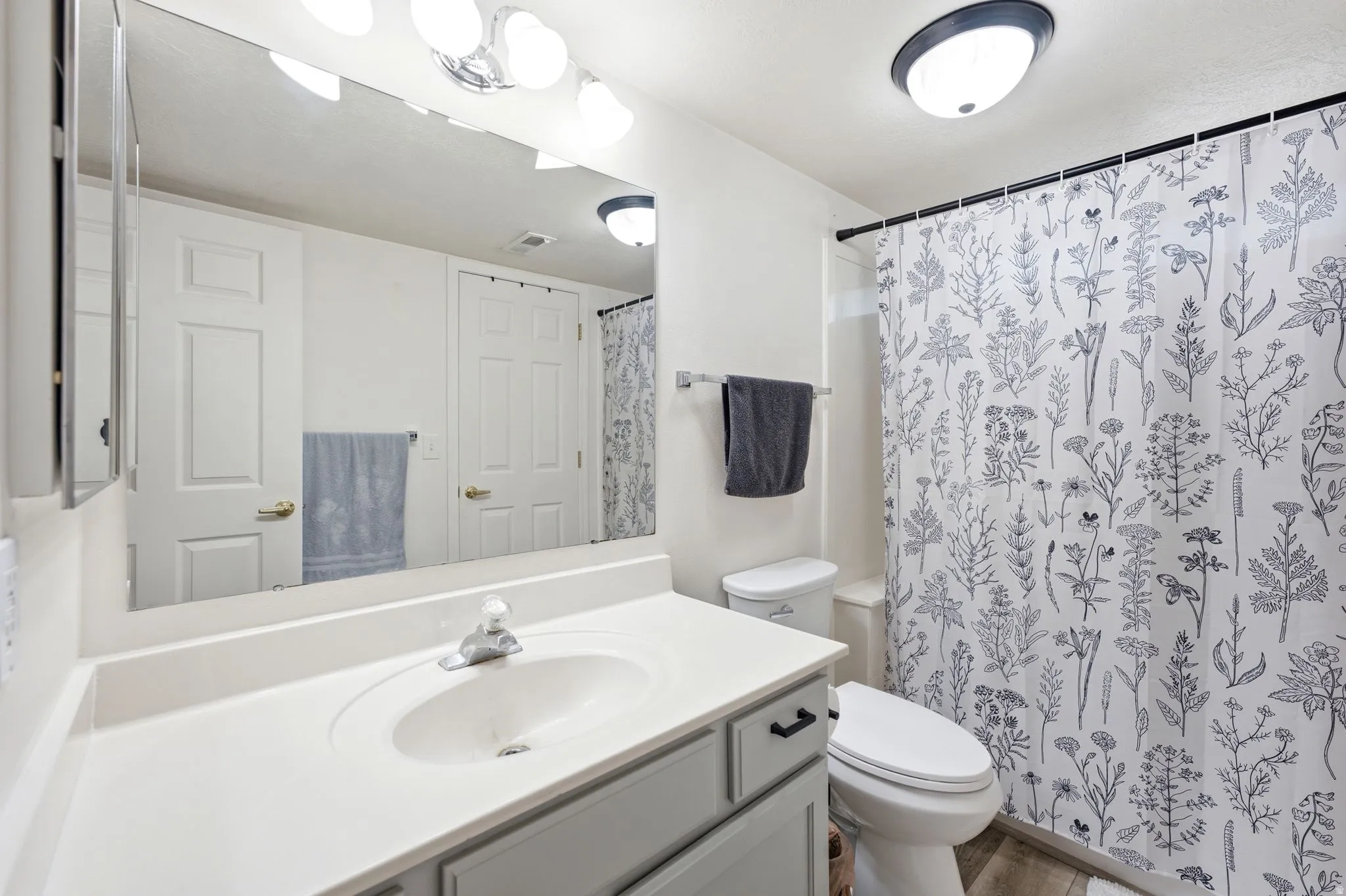 Bathroom vanity featuring a single basin sink, light-toned countertop, and light gray cabinetry with dark hardware