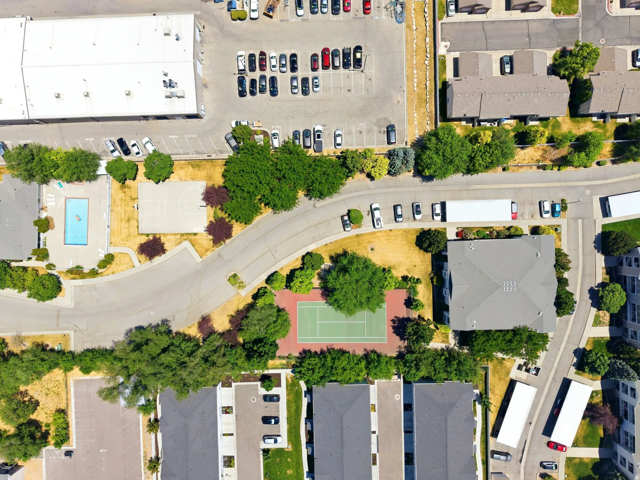 Aerial view showcasing a community with multiple residential buildings, a tennis court, a basketball court, and a swimming pool