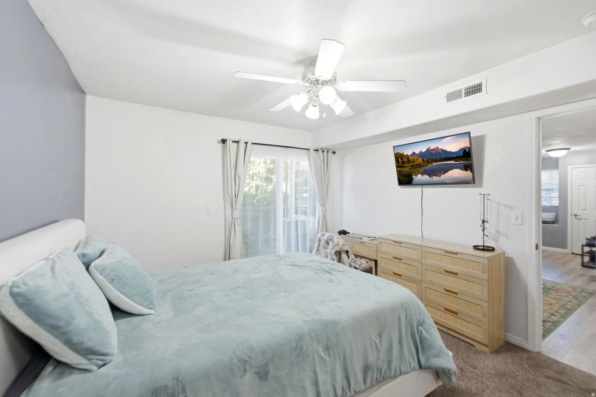 Master bedroom featuring a ceiling fan, light-toned carpeting, and a sliding glass door with sheer and blackout curtains