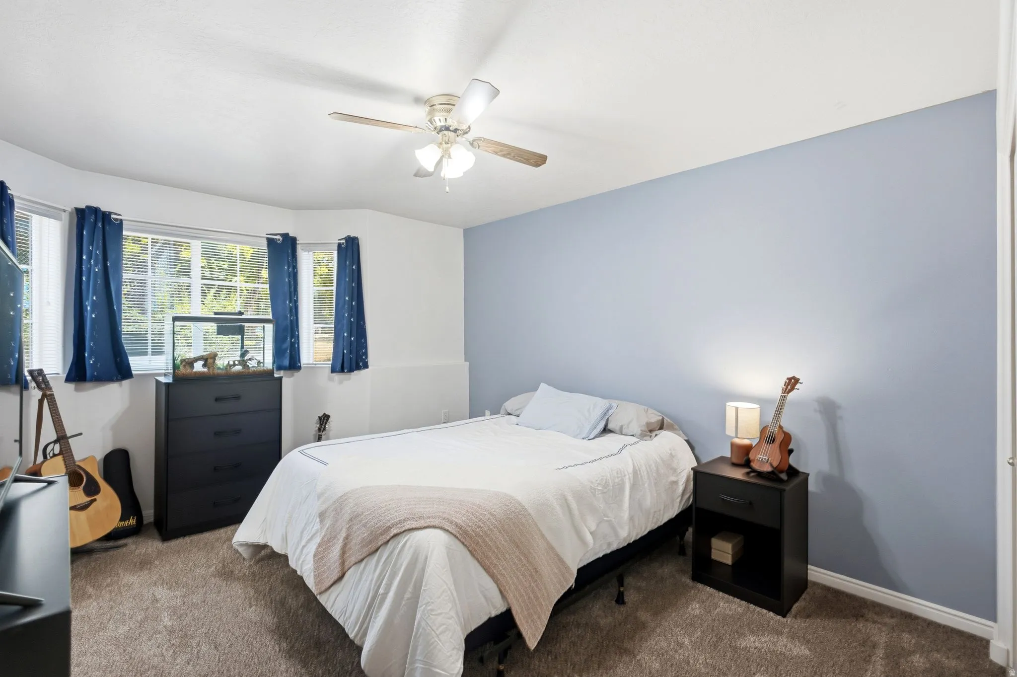 Carpeted room featuring a ceiling fan with integrated lighting, a bay window with multiple panes, a contrasting accent wall, and white baseboards