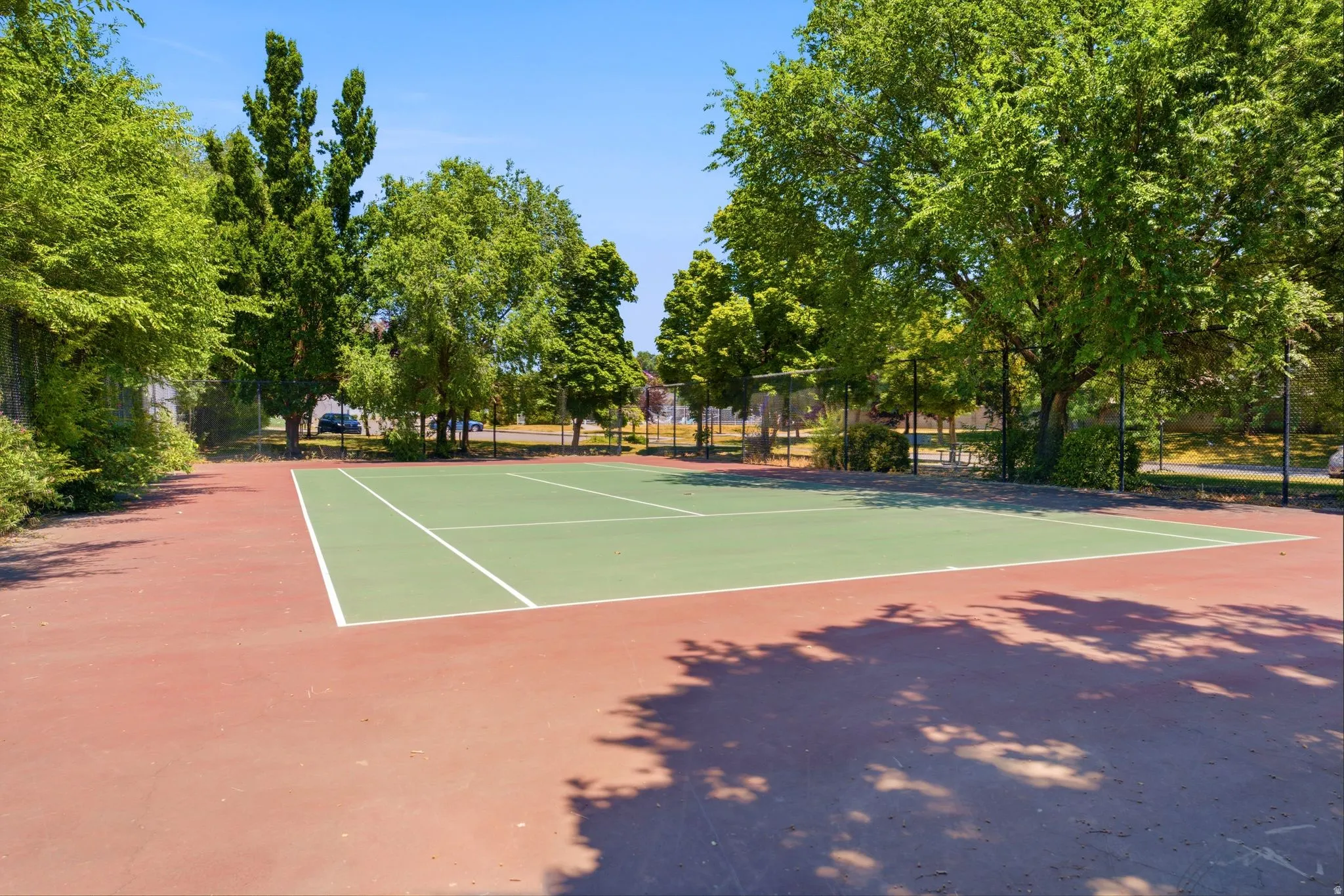 Regulation-size tennis court featuring a green playing surface and red perimeter