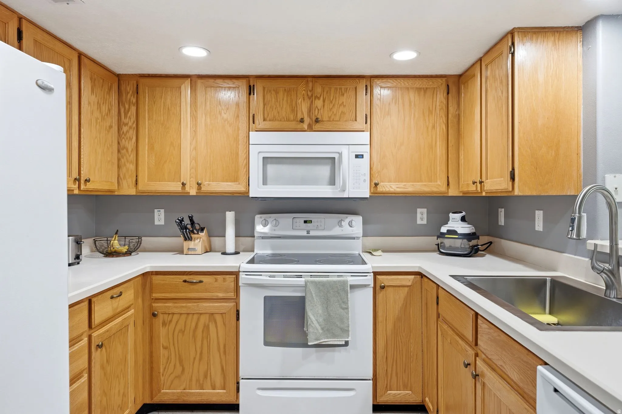 U-shaped kitchen featuring wood-finish cabinetry, white countertops, a double basin stainless steel sink, and recessed lighting